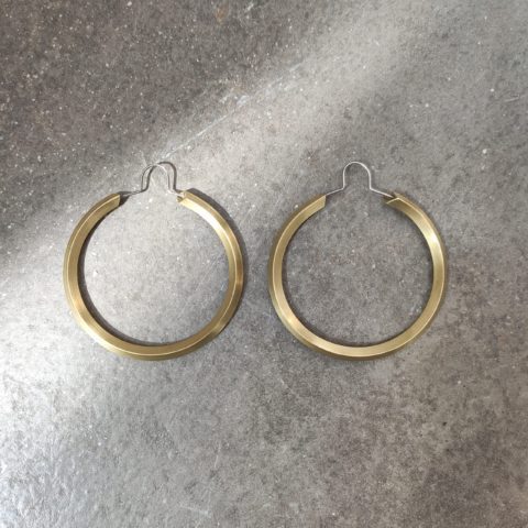 Angular round brass hoops with a stainless steel upside down u earring hook, sit on a grey background with a beam of light across the top right corner to the bottom left corner