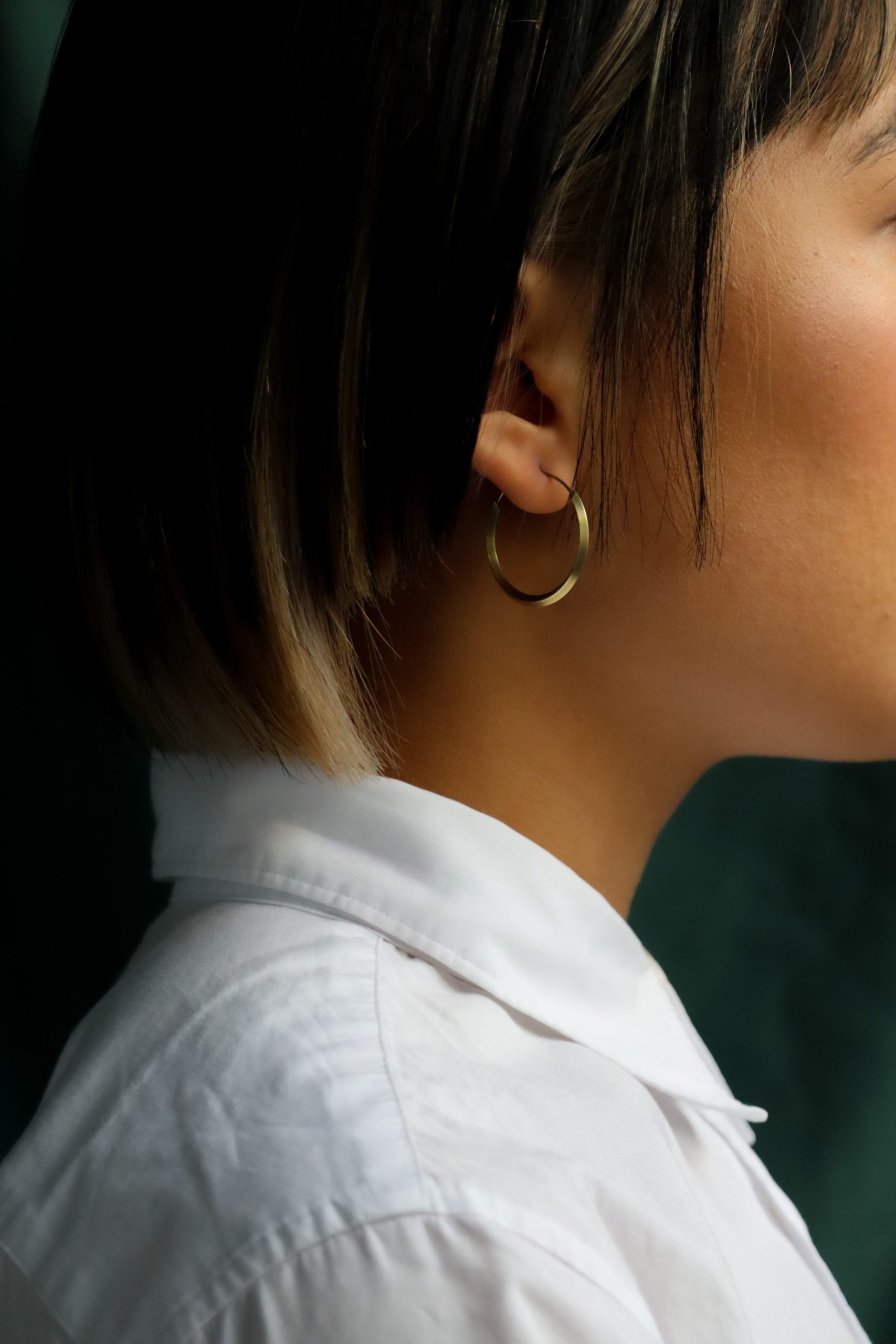 Side view of young woman with short hair, white collared shirt shoulders up wearing 30mm brass hoops