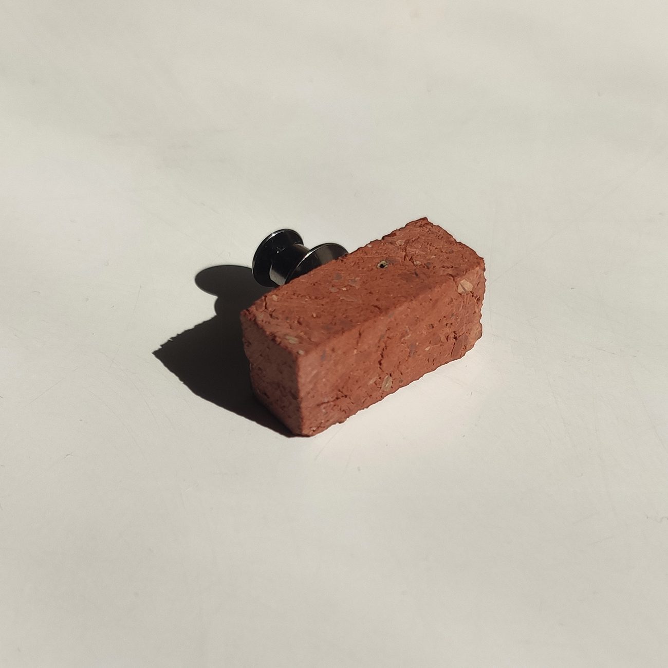 Little red brick with pin attached on off white background